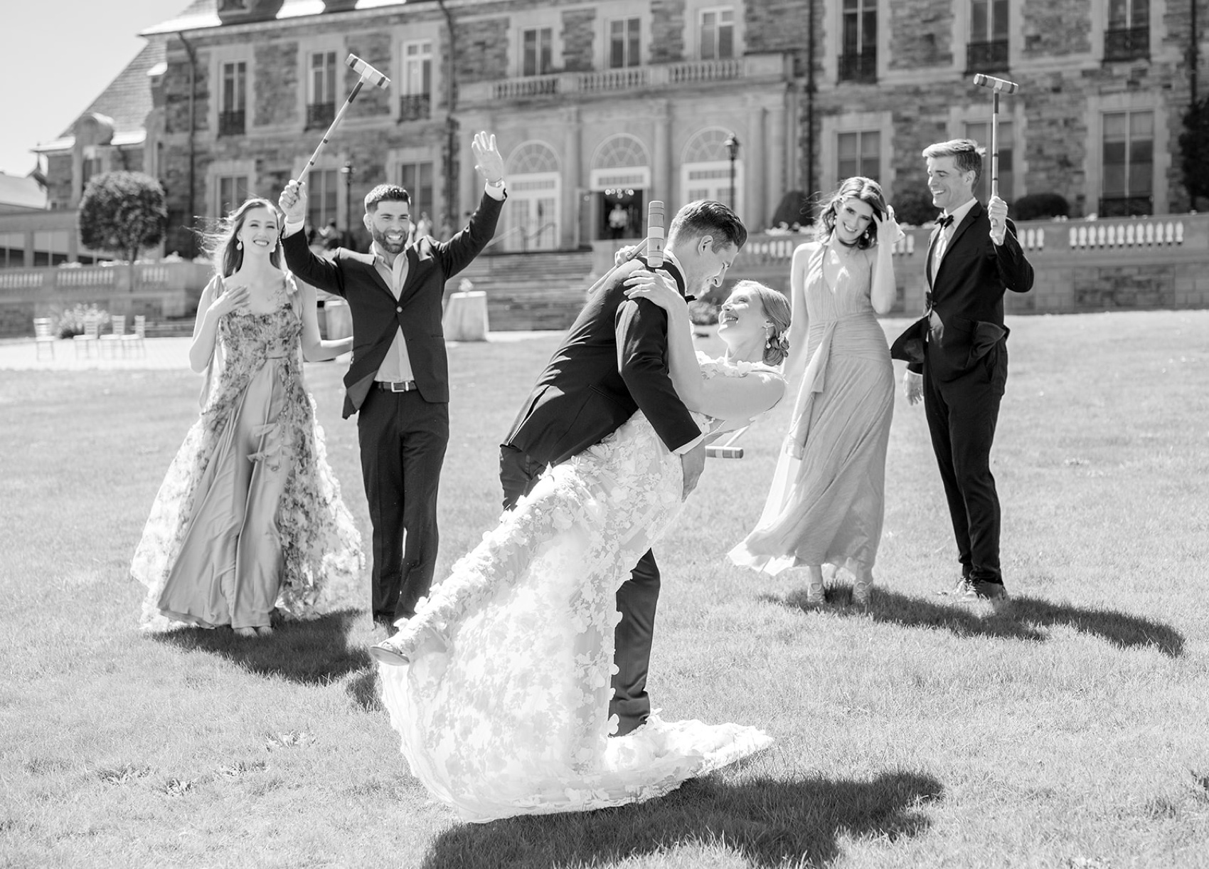 A groom dips his bride for a happy kiss while playing crochet with their bridal party in the aldrich mansion wedding venue lawn