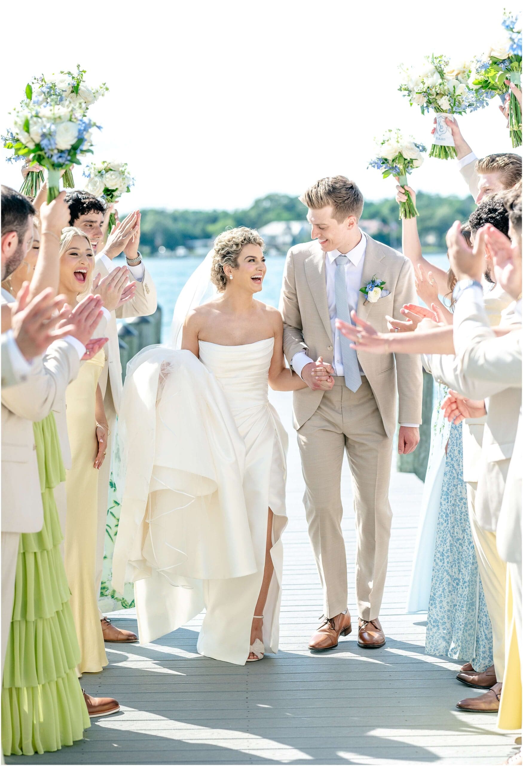 Newlyweds walk up the aisle with huge smiles as their wedding party lines it with cheers
