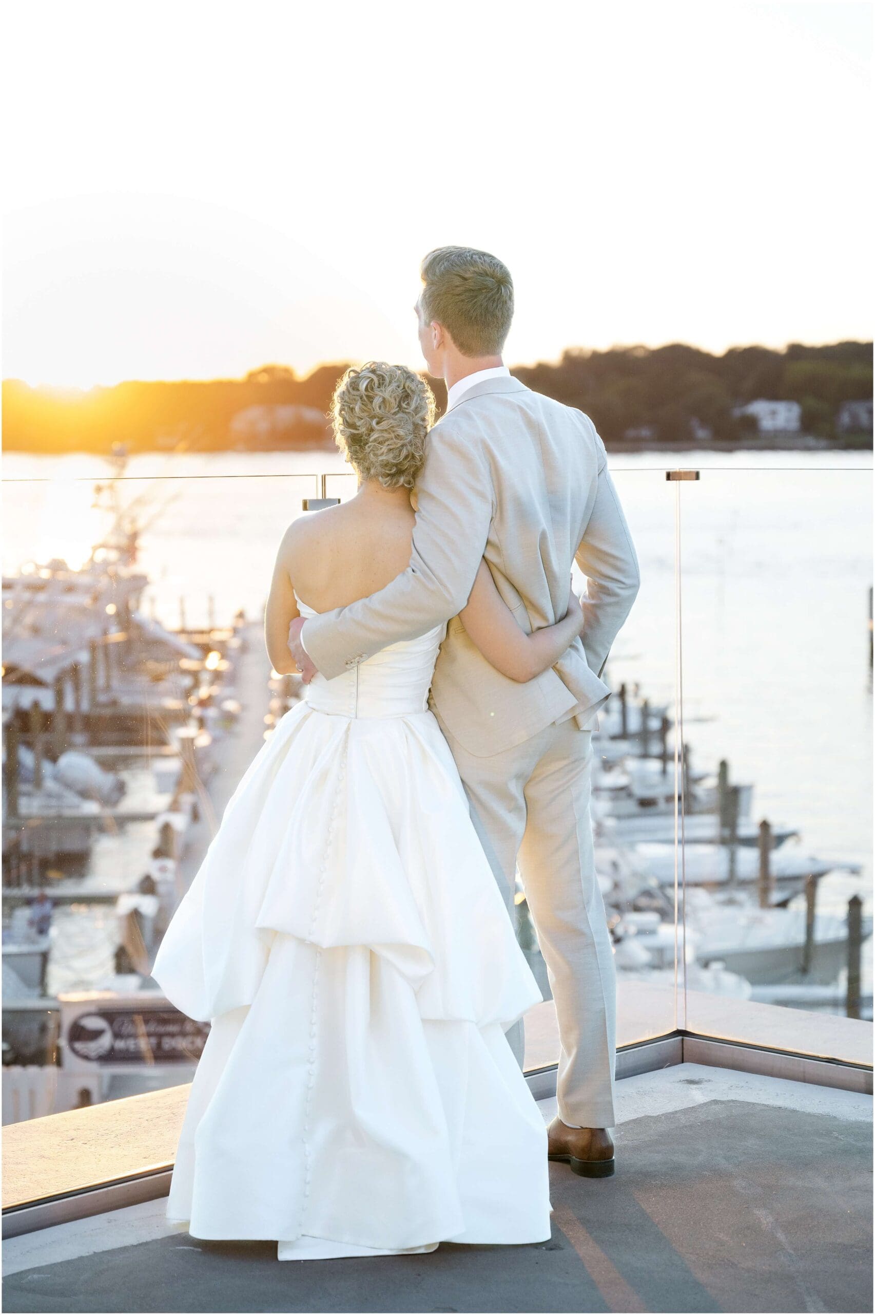 Newlyweds hold each other and watch the sunset over the marina during their Clarks Landing Yacht Club wedding