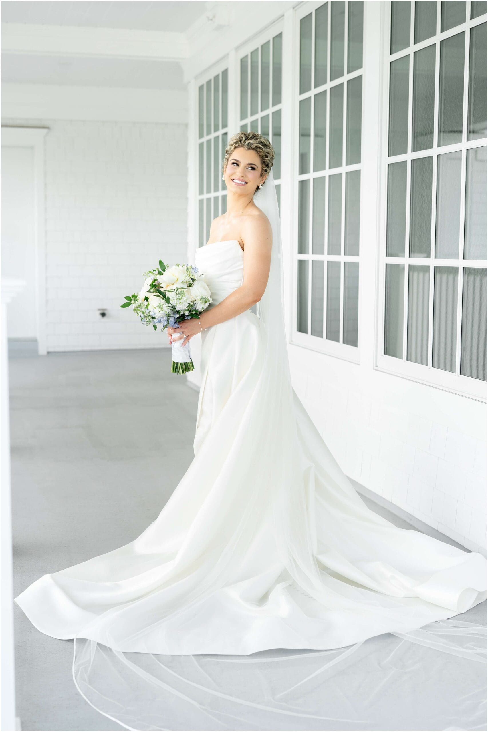 A happy bride smiles over her shoulder while standing on a porch during her Clarks Landing Yacht Club wedding