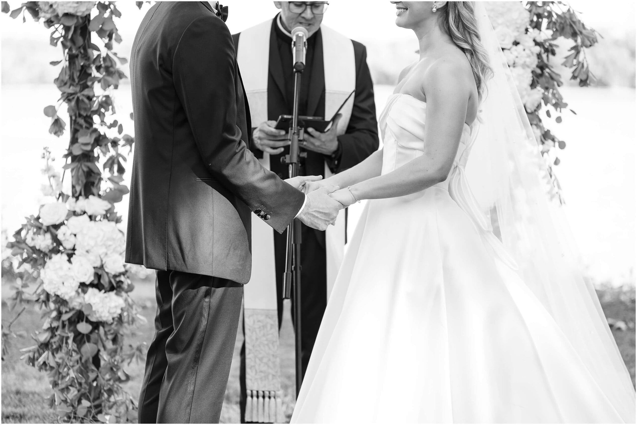 A black and white image of the bride and groom's hands holding each other during their outdoor ceremony